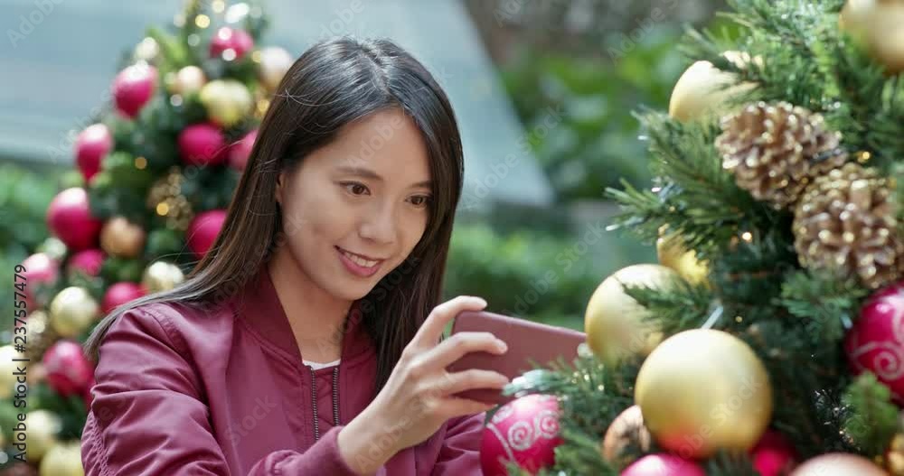 Woman take photo on cellphone with Christmas tree decoration Woman take photo on cellphone with Christmas tree decoration