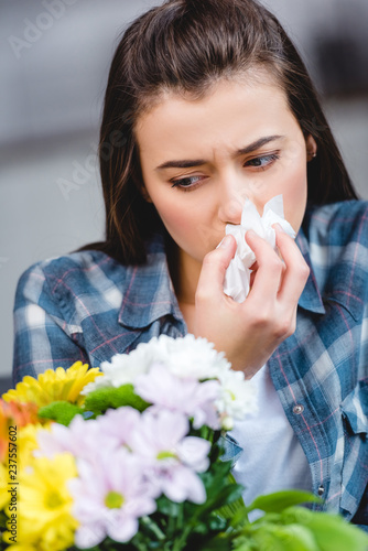 young woman with allergy holding facial tissue and looking at flowers
