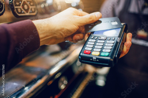 One hand hold machine for cards white another hold dark card for paying money. Men stand at coffee machine. photo