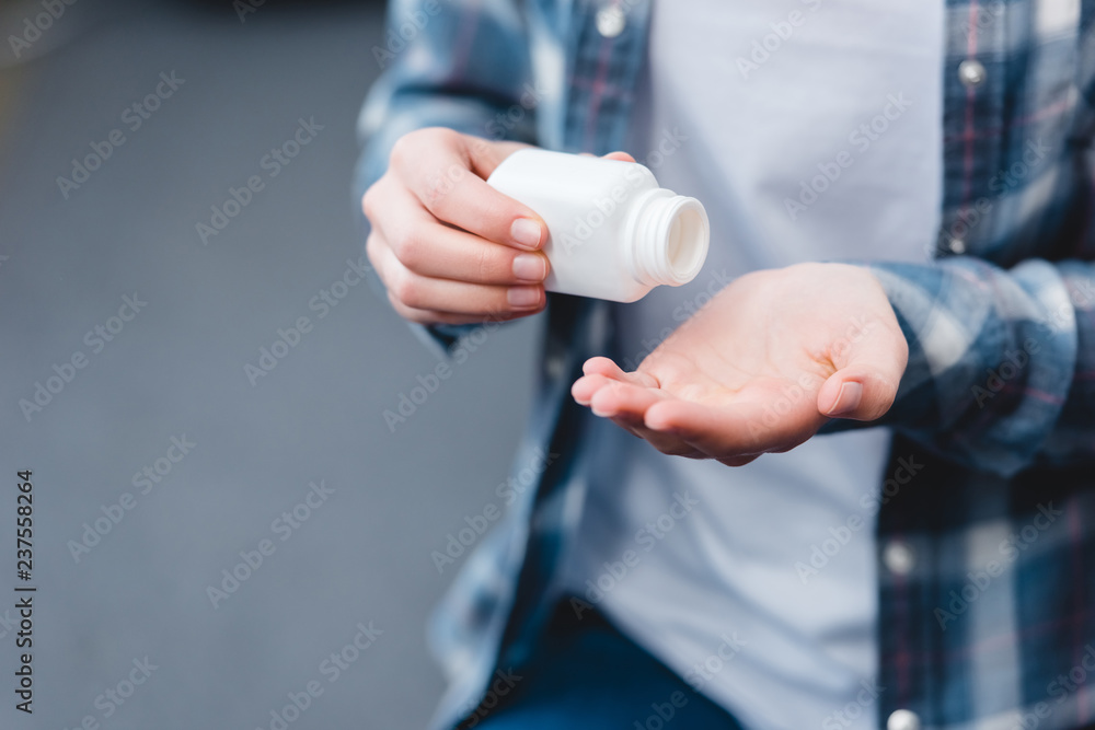 cropped shot of young woman holding container with pills