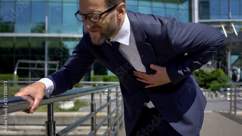 Worried businessman having heart attack outdoors, strong chest pain, first aid