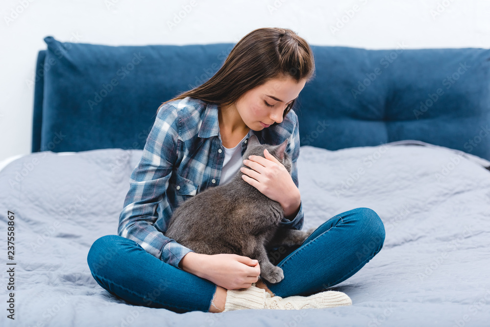 beautiful young woman sitting on bed with cute british shorthair cat