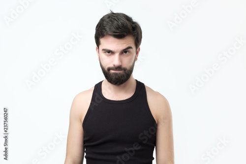Doubtful bearded young in black t-shirt man has doubtful expression on face. Negative facial emotion