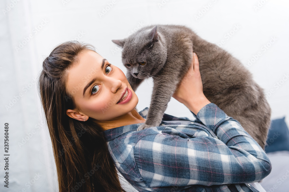 beautiful young woman holding british shorthair cat and smiling at camera