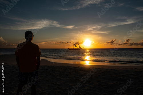 Silhouette of a Man Watching Sunset Over the Ocean with a Sailboat Passing the Horizon
