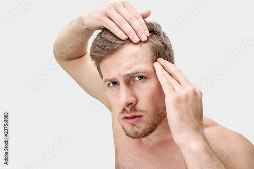 Portrait of young man looking on camera. He hold hands on hair. He is worried. Isolated on white background.