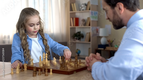 Little daughter thinking over next move, playing chess with father, strategy