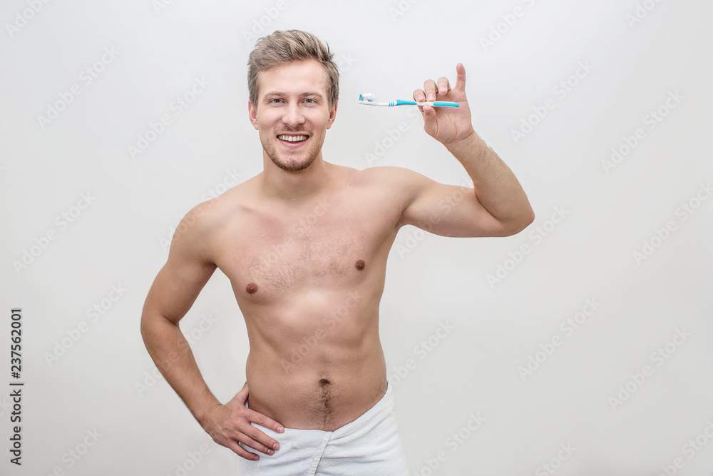 Happy and healthy young man hold tooth brush with toothpaste on it. Guy look on camera and smile. He shows beautiful smile. Guy is shirtless. Isolated onwhite background. Happy and healthy young man hold tooth brush with toothpaste on it. Guy look on camera and smile. He shows beautiful smile. Guy is shirtless. Isolated onwhite background.
