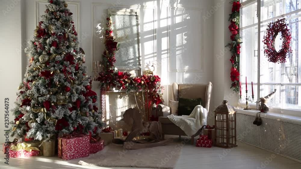 White room interior in red tones with New Year tree decorated, present boxes and artificial fireplace White room interior in red tones with New Year tree decorated, present boxes and artificial fireplace