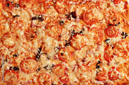 Close-up of hot pizza with melting cheese, ham, mushrooms and tomatoes. Food texture and background. Top view