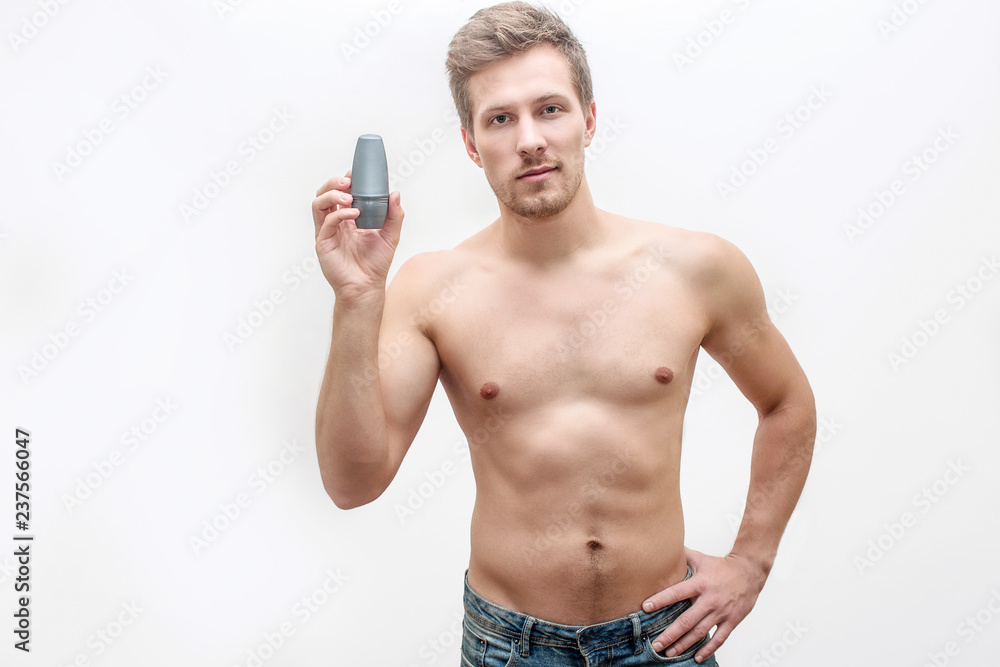 Shirtless young man hold deodorant in hand. He shows it. Guy look straight. He pose. Isolated on white background. Shirtless young man hold deodorant in hand. He shows it. Guy look straight. He pose. Isolated on white background.