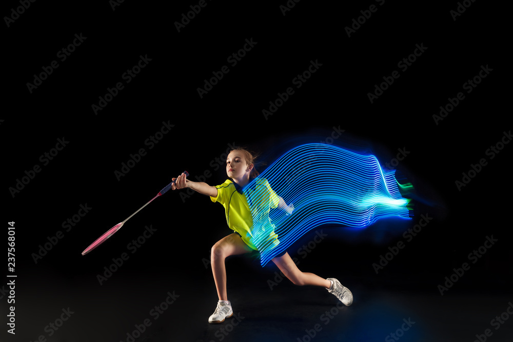 The one caucasian young teenager girl playing badminton at studio. The female teen player on black background in motion with flashes of light