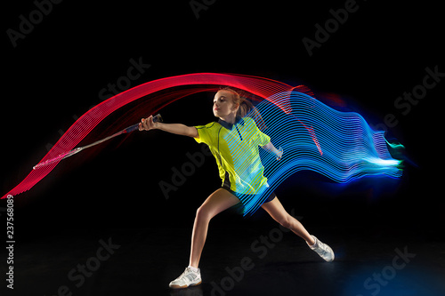 The one caucasian young teenager girl playing badminton at studio. The female teen player on black background in motion with flashes of light © master1305
