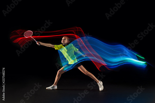 The one caucasian young teenager girl playing badminton at studio. The female teen player on black background in motion with flashes of light © master1305