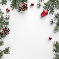 Creative frame made of Christmas fir branches on white paper background with red decoration, pine cones. Xmas and New Year theme. Flat lay, top view
