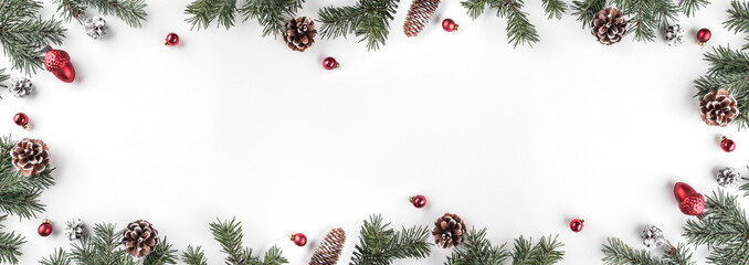 Creative frame made of Christmas fir branches on white background with red decoration, pine cones. Xmas and New Year theme. Flat lay, top view, wide composition