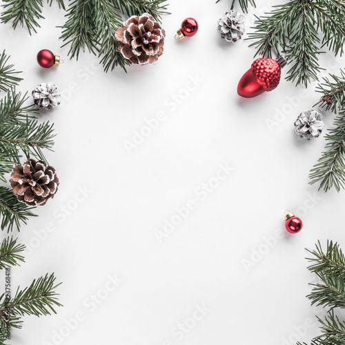 Creative frame made of Christmas fir branches on white paper background with red decoration, pine cones. Xmas and New Year theme. Flat lay, top view