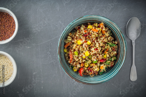 Quinoa salad bowl with various vegetables: green beans, carrot, corn, bell pepper, peas and two bowls with red and white quinoa seeds on grey background. Top view, copy space.