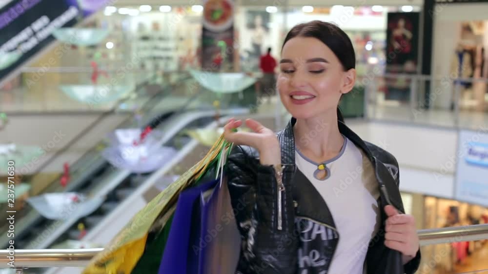 Portrait of a happy smiling girl with paper bags in the mall on the background of the escalator. Happy girl with lots of shopping walks through the shopping center. Portrait of a happy smiling girl with paper bags in the mall on the background of the escalator. Happy girl with lots of shopping walks through the shopping center.