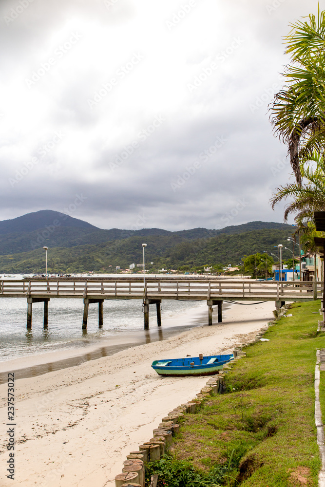 Wooden pier of Morrinhos beach, with wooden fishing boat and Zimbros beach in the background, Bombinhas, Santa Catarina