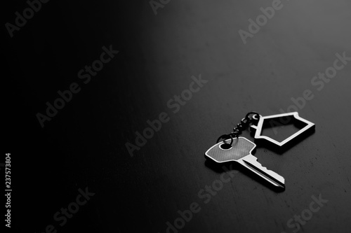 Home key with house keyring on black wood table in dark tone, real estate concept