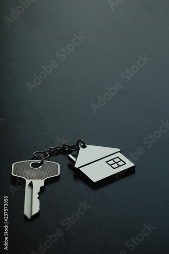 Home key with house keyring on black wood table in dark tone, real estate concept