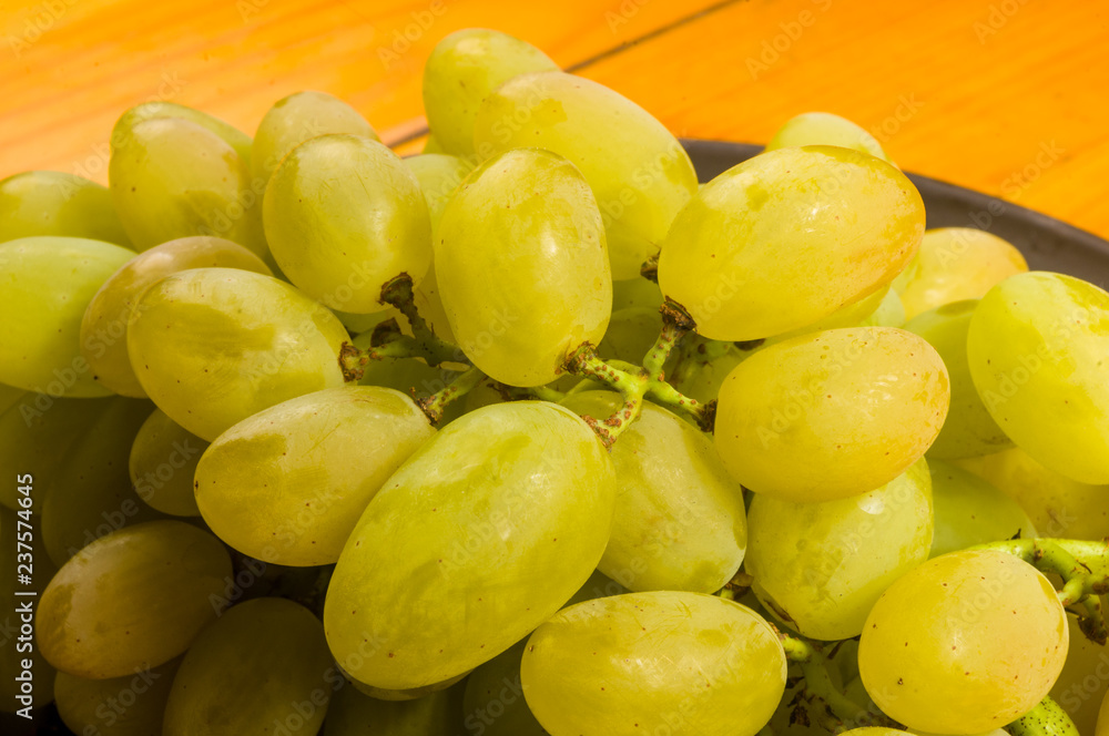large brush of green grapes in a dark ceramic plate on a wooden background