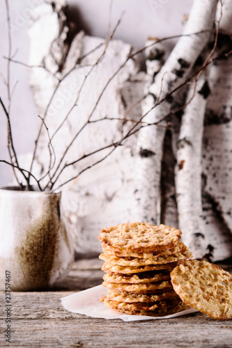 Havreflarn - scandinavian crispy slim oatmeal cookies, birch branches and bark on old wooden background. Fast and easy scandinavian pastry. Cozy winter treat. Hygge. Fika. Christmas