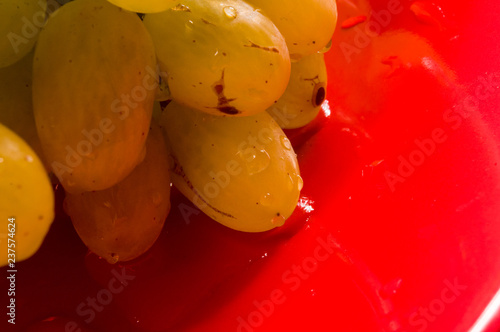 large brush of green grapes in a red ceramic plate on a wooden background