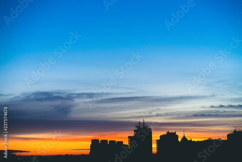 Cityscape with wonderful varicolored vivid dawn. Amazing dramatic blue sky with purple and violet clouds above dark silhouettes of city buildings. Atmospheric background of orange sunrise. Copy space.