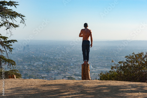 Murais de parede Man standing on a dead tree stump in Griffith park looking out over the city of