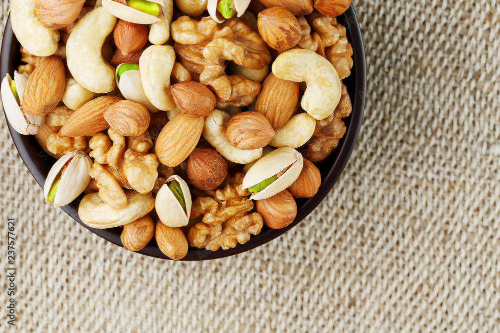 Mix of different nuts in a wooden cup against the background of fabric from burlap. Nuts as structure and background, macro. Top view. Mix of different nuts in a wooden cup against the background of fabric from burlap. Nuts as structure and background, macro. Top view.