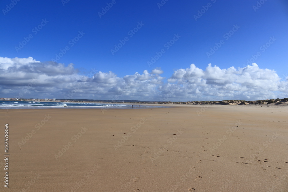 sand sea with people in background and sky with white clouds
