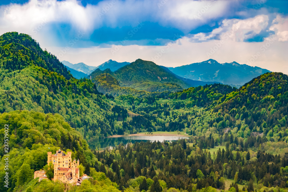 Beautiful landscape view of the Hohenschwangau Castle and lake Schwansee surrounded by forest and the Alps in the background. The castle is near the town of Füssen in southwestern Bavaria, Germany.