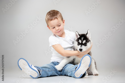 Portrait of a joyful little boy having fun with siberian husky puppy on the floor at studio. The animal, friendship, love, pet, childhood, happiness, dog, lifestyle concept