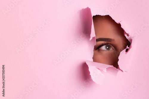 Girl with bright eyes make up looks through hole of pink paper. Business card of artist, beauty concept. Ready to new year party. Cosmetics sale. Beauty salon advertising banner with copy space © jchizhe