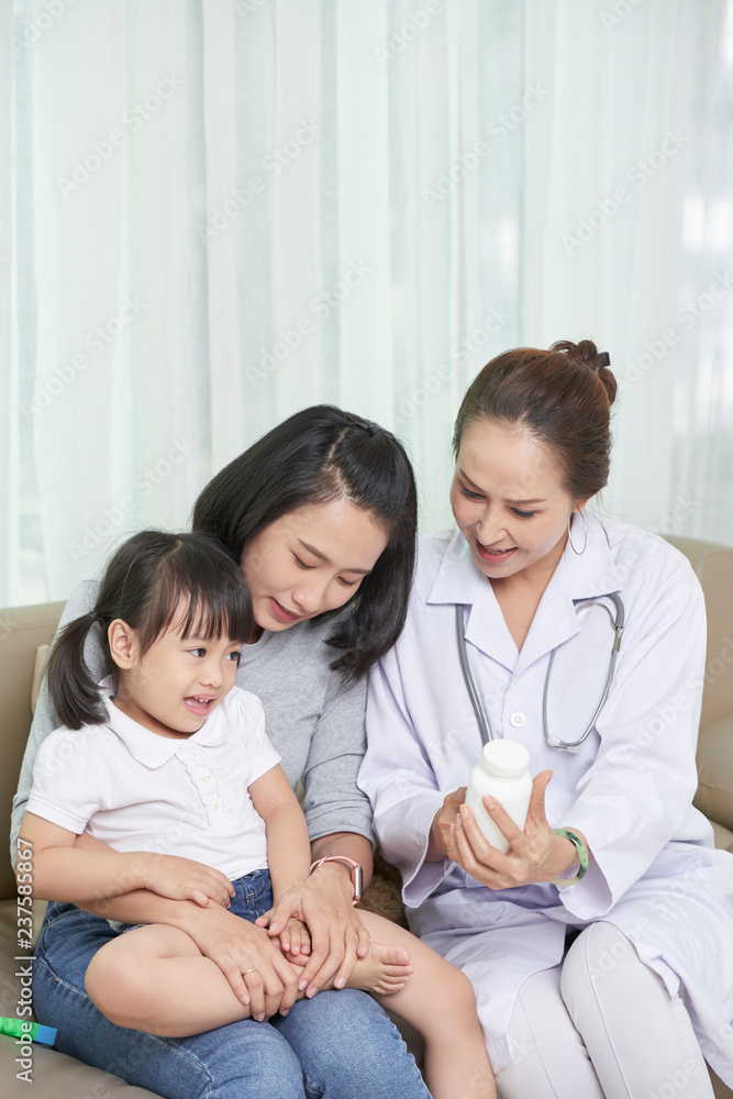 Mature Vietnamese pediatrician prescribing vitamins to little girl Mature Vietnamese pediatrician prescribing vitamins to little girl