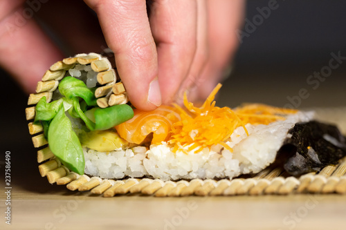 Process of rolling up sushi roll with salmon using bamboo mat, viewed from the side in closeup