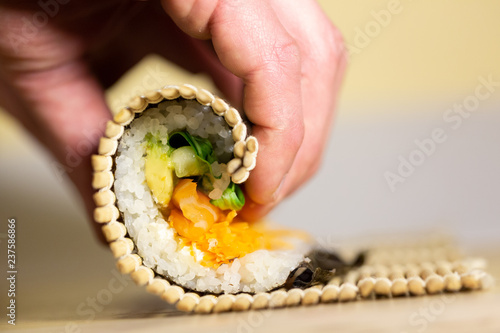 Process of rolling up sushi roll with salmon using bamboo mat, viewed from the side in closeup