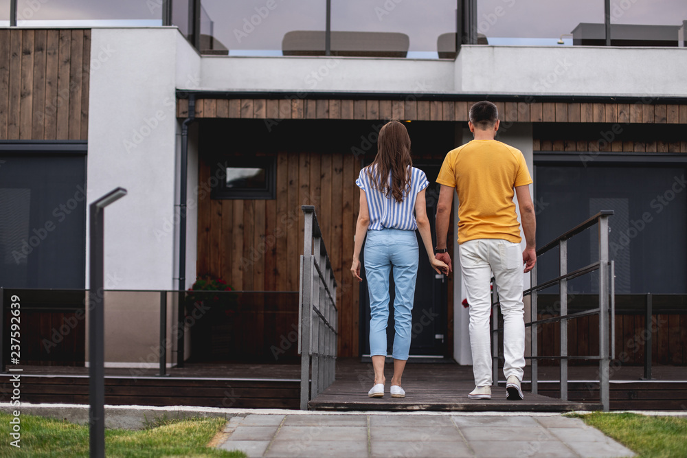 Full length portrait of backs of couple. They holding hands and walking to home. Copy space on left side Full length portrait of backs of couple. They holding hands and walking to home. Copy space on left side