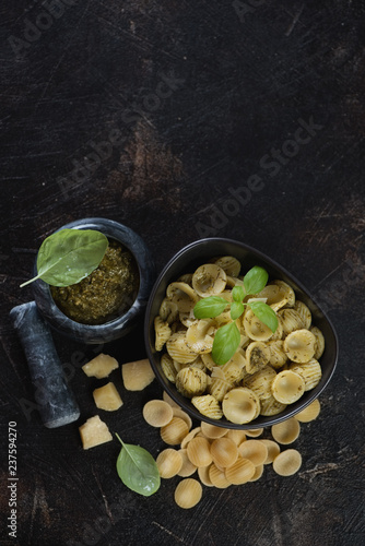 Bowl of orecchiette served with freshly made basil pesto sauce, flatlay with space on a dark brown stone background