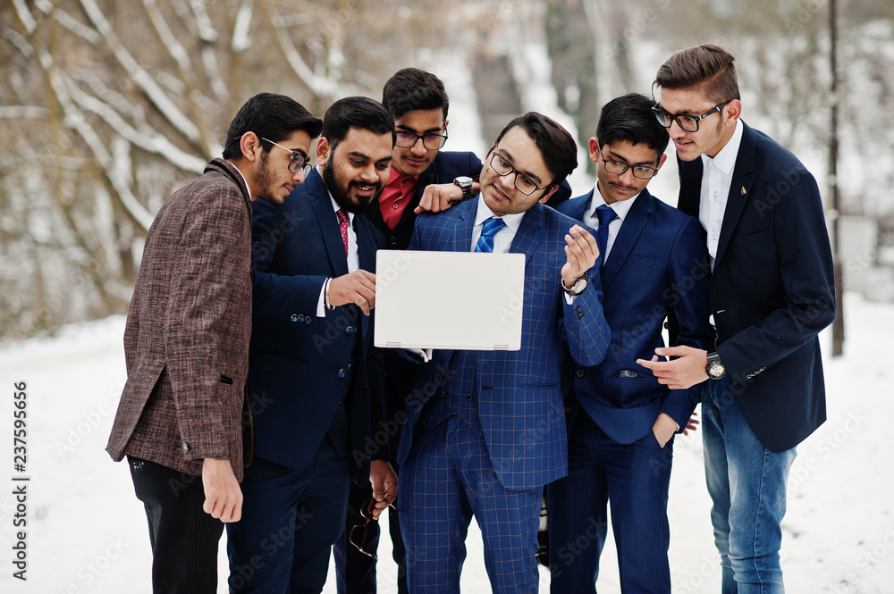 Fototapeta premium Group of six indian businessman in suits posed outdoor in winter day at Europe, looking on laptop.