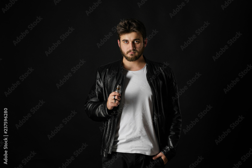 Man with vaping mod exhaling steam at black studio background. Bearded guy smoking e-cigarette to quit tobacco. Vapor and alternative nicotine free smoking concept Man with vaping mod exhaling steam at black studio background. Bearded guy smoking e-cigarette to quit tobacco. Vapor and alternative nicotine free smoking concept