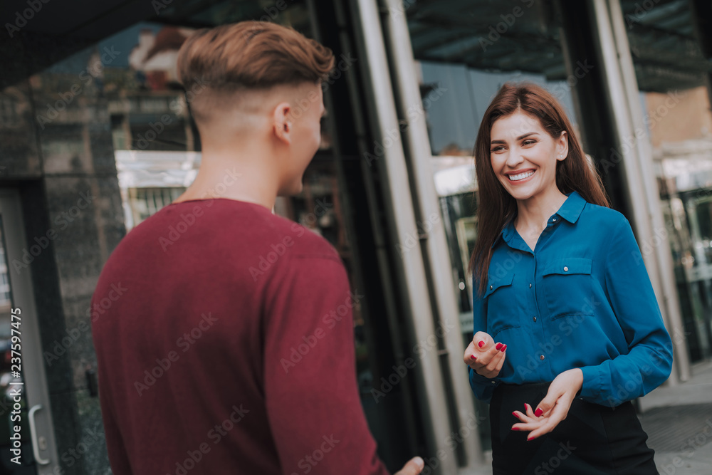 Concept of friendly communication. Waist up portrait of young cheerful man and woman meeting near business center and discussing something Concept of friendly communication. Waist up portrait of young cheerful man and woman meeting near business center and discussing something