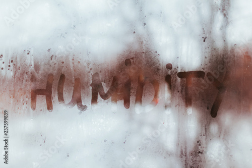 Humidity word written on wet window. High level of dampness in apartment.