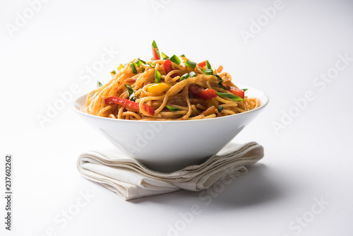 Schezwan Noodles or vegetable Hakka Noodles or chow mein is a popular Indo-Chinese recipes, served in a bowl or plate with wooden chopsticks. selective focus photo