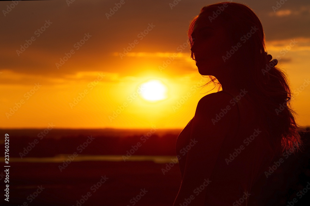 silhouette of a beautiful romantic girl at sunset , face profile of young woman with long hair in hot weather