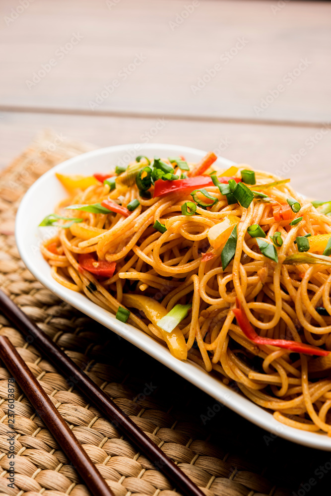 Schezwan Noodles or vegetable Hakka Noodles or chow mein is a popular Indo-Chinese recipes, served in a bowl or plate with wooden chopsticks. selective focus Schezwan Noodles or vegetable Hakka Noodles or chow mein is a popular Indo-Chinese recipes, served in a bowl or plate with wooden chopsticks. selective focus