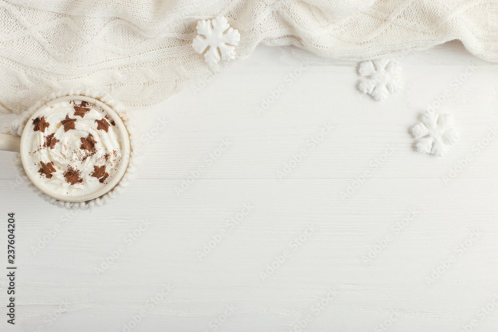 A cup of hot winter drink with whipped cream and a dusting powder with an asterisk, white snowflakes and knitted scarf on a wooden table. Christmas concept in bright colors. Copy space.