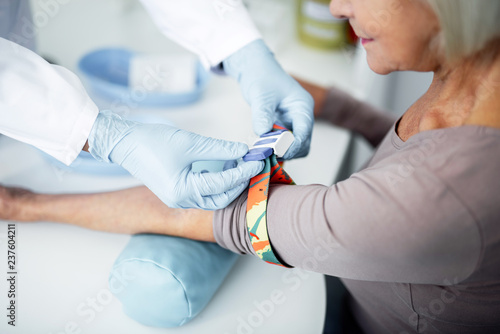 Professional practitioner wearing rubber gloves and putting colorful garrot on the arms of his patient